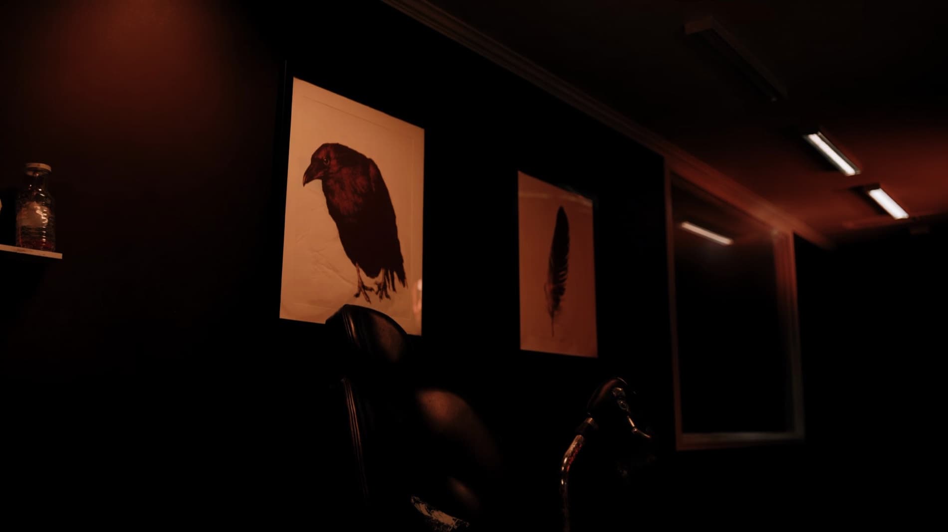 Dark studio wall with framed raven artwork under rust-orange glow
