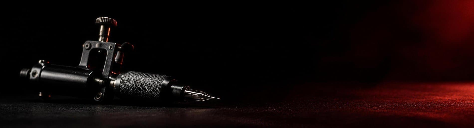 Wide macro of a matte black rotary tattoo machine on a dark workstation, vermillion haze behind it