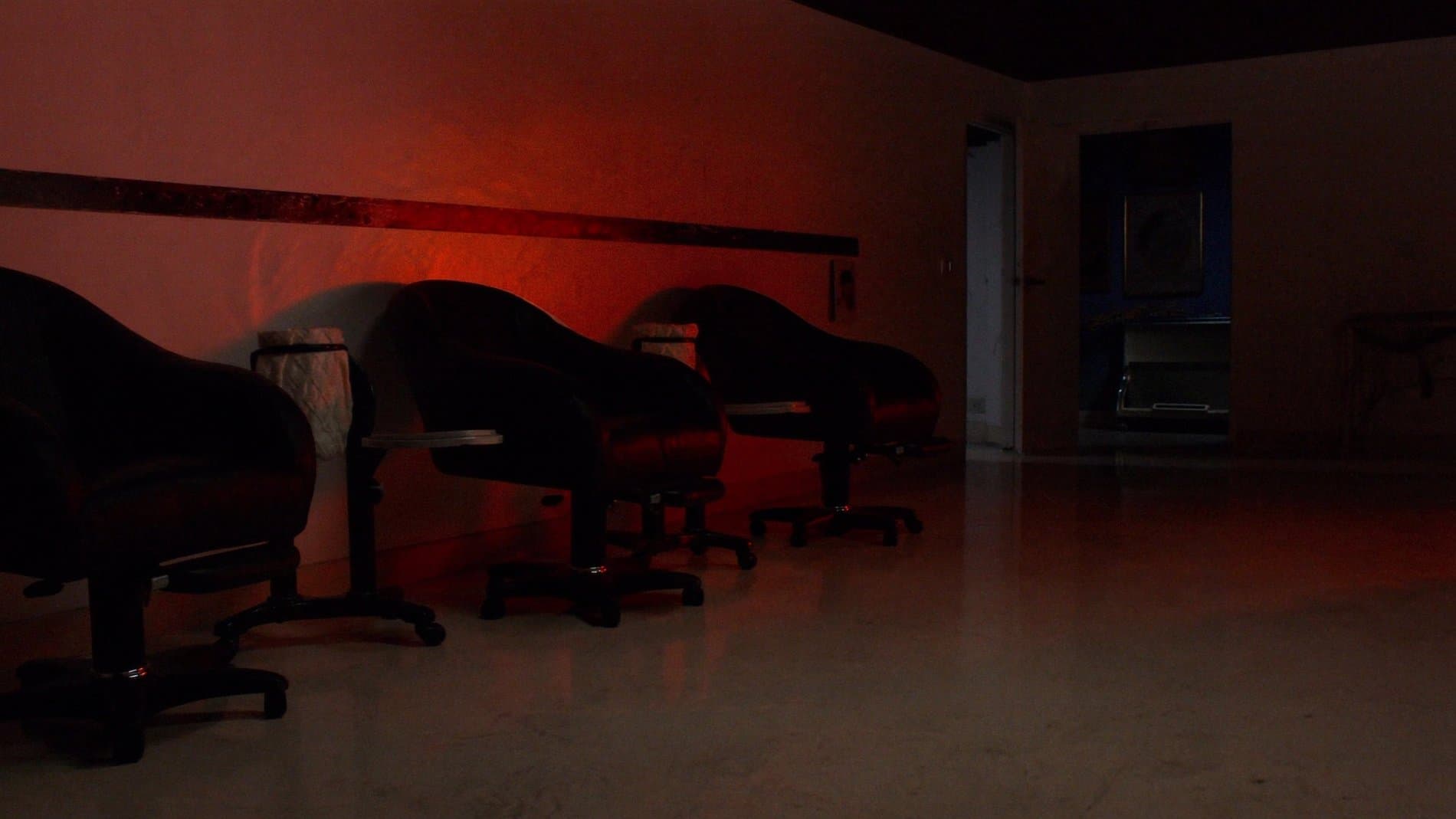 An empty tattoo studio at night, chairs along a wall under a single warm vermillion light