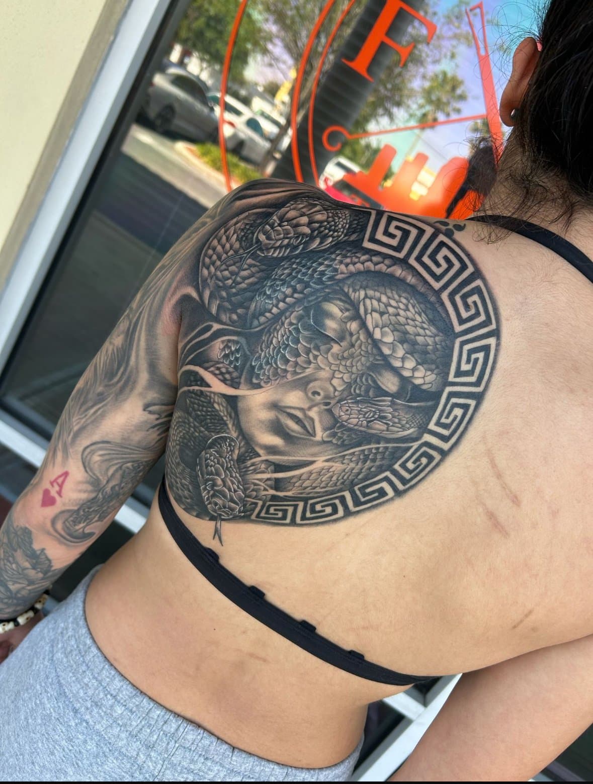 Black and grey Medusa and serpent back piece framed by a Greek key border