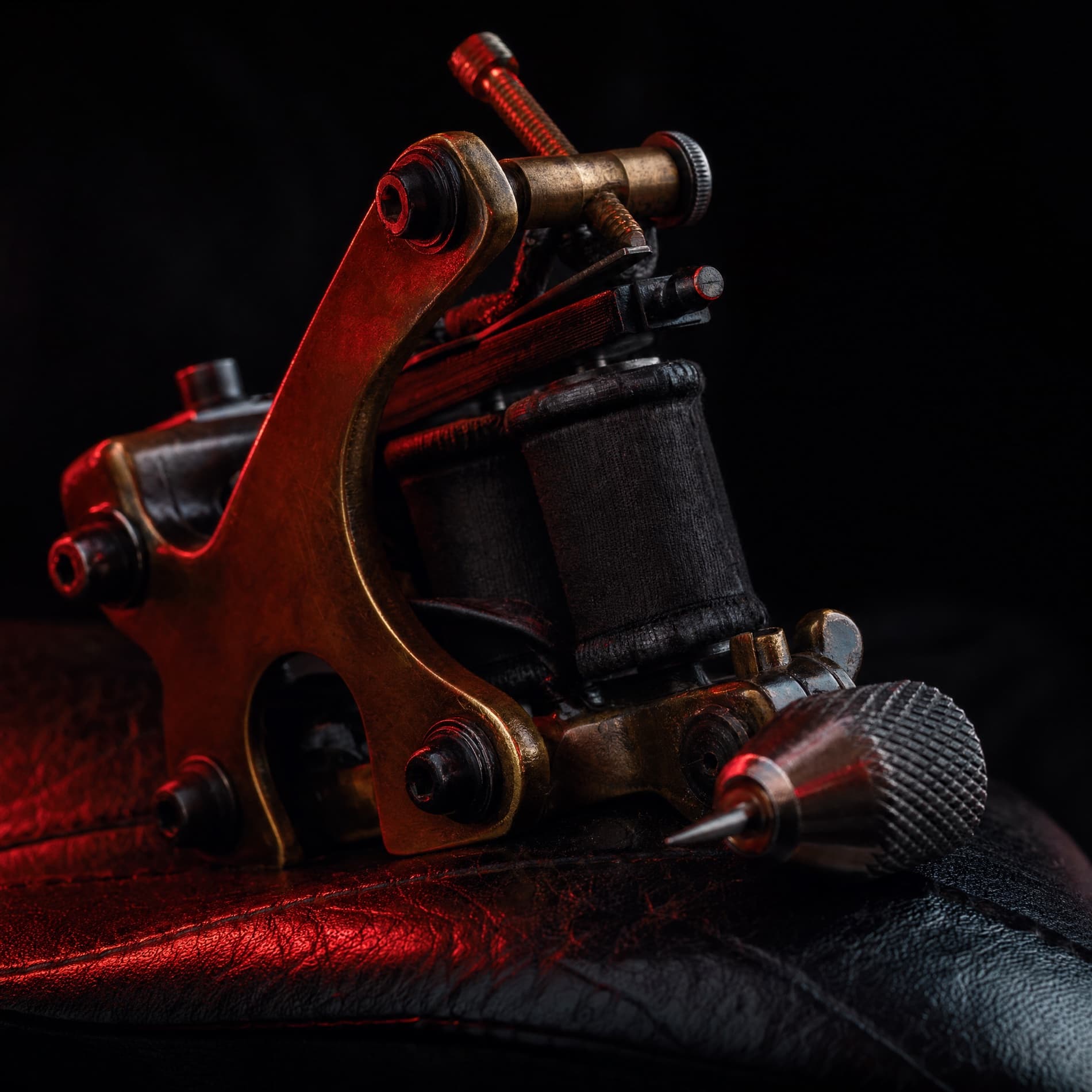 Vintage brass coil tattoo machine on worn leather in red light