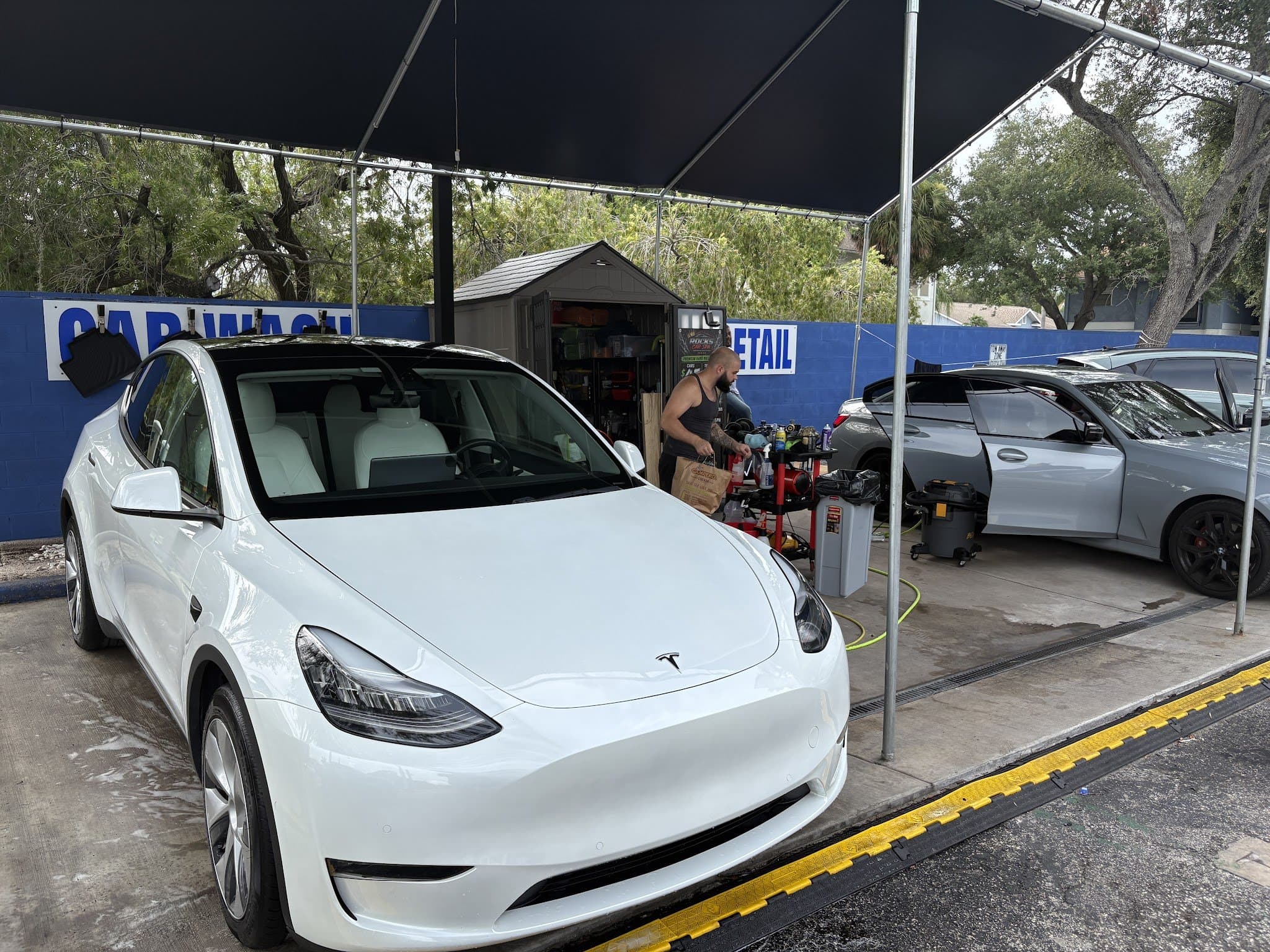 A freshly hand-washed white Tesla Model Y under the wash canopy at Rock's Car Spa on Memorial Hwy in Tampa