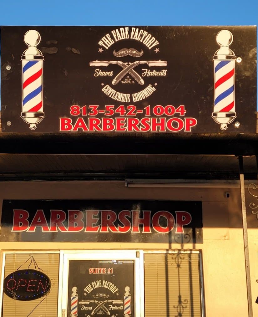 The Fade Factory street sign with barber poles and phone number neon